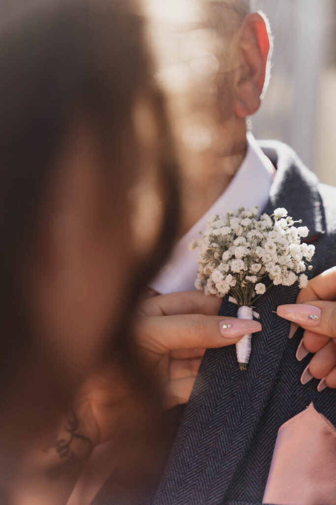 A candid shot of a father getting his buttonhole at his daughter's wedding, taken in a documentary style by a photographer in Hampshire.